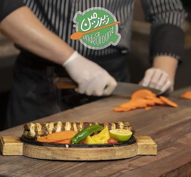 آشپز کافه رستوران زیرزمین در حال برش سبزیجات برای غذای کباب سینی داغ با هویج، فلفل و لیمو. تجربه آشپزی حرفه‌ای.