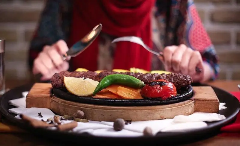 تجربه کباب کوبیده لذیذ در کافه رستوران زیرزمین: مشتری در حال لذت بردن از غذای سنتی ایرانی شامل کباب، گوجه و فلفل است.