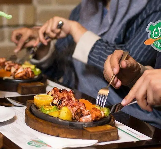 تصویری جذاب از مشتریان کافه رستوران زیرزمین که کباب مرغ و سبزیجات تازه را روی سینی داغ سنگی میل می‌کنند، تجربه‌ای فراموش‌نشدنی.