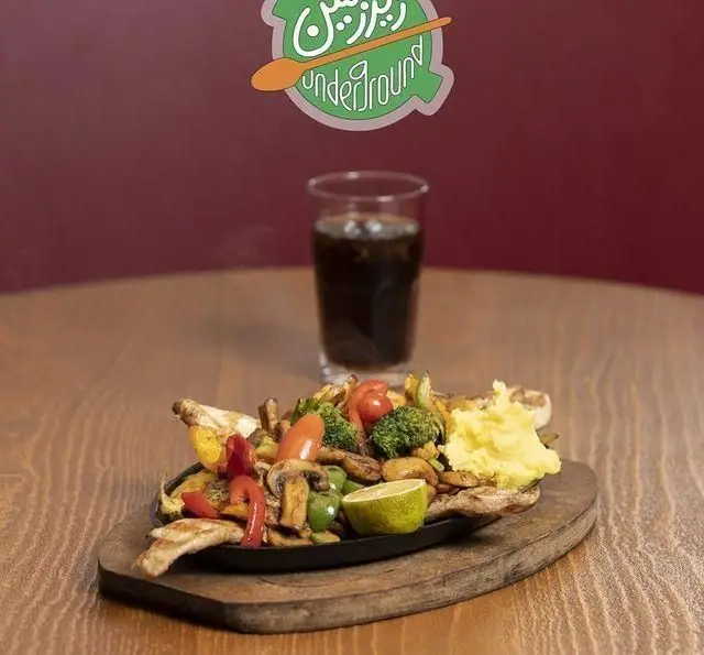 بشقاب داغ مرغ با سبزیجات (کلم بروکلی، فلفل، قارچ) و پوره سیب زمینی، همراه با نوشیدنی در کافه رستوران زیرزمین.