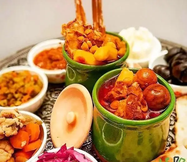 تصویری جذاب از میز غذای رستوران سنتی دیزی میزی شامل دو کاسه دیزی یا آبگوشت، مخلفات خوشمزه ایرانی و ترشیجات.