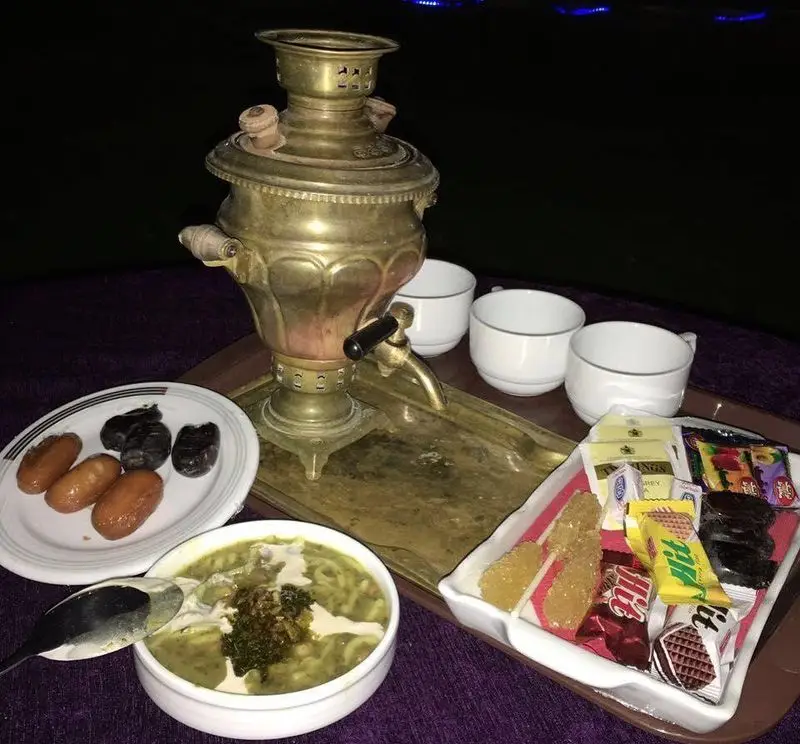 سماور سنتی برنجی، آش رشته، خرما و شیرینی‌های بامیه در رستوران باغ گلستان، همراه با چای و شکلات، لذت شام و دورهمی شبانه.