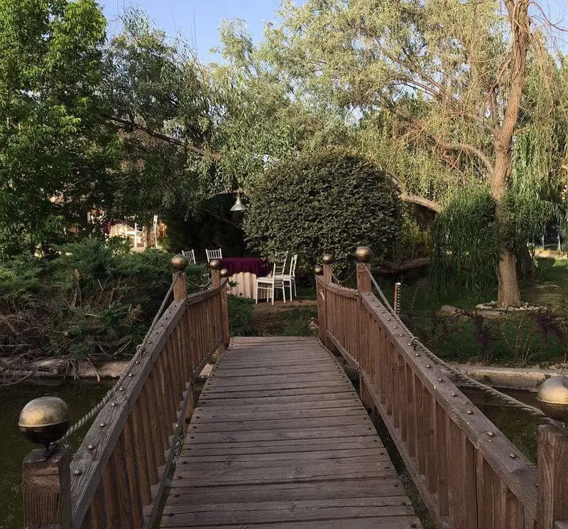 چشم‌انداز دلنشین از پل چوبی ورودی به فضای سبز و زیبای رستوران باغ گلستان با میز و صندلی چیدمان شده برای میزبانی خاص.