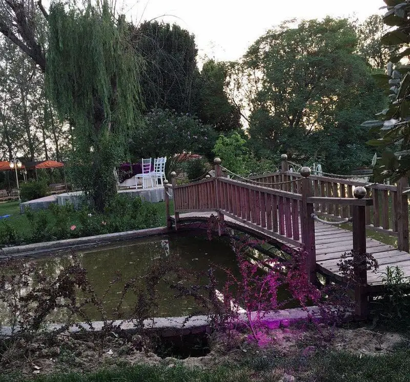 رستوران باغ گلستان: نمایی زیبا از فضای سبز و آرام باغ با برکه، پل چوبی و نشیمن، ایده‌آل برای پذیرایی.