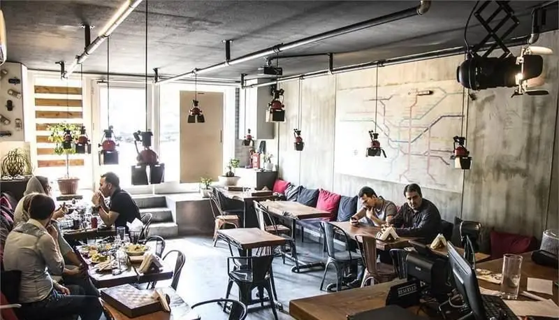 نمای داخلی ایستگاه ساندویچ: مشتریان در حال صرف غذای خوشمزه در فضایی با دکوراسیون صنعتی و نقشه مترو روی دیوار.