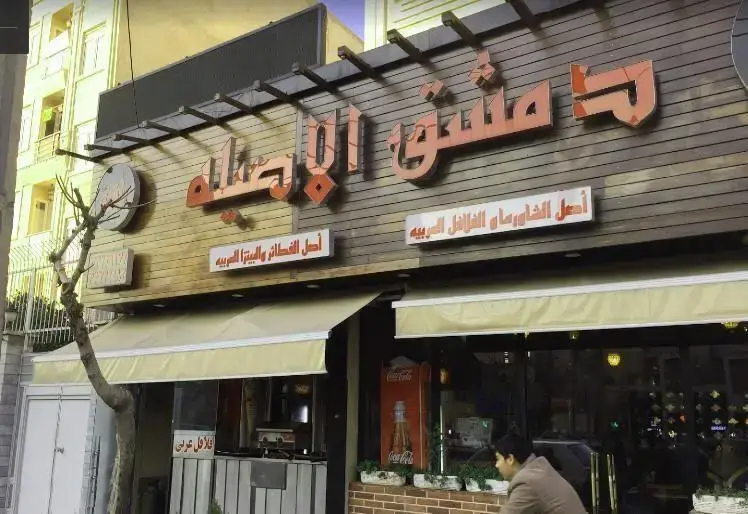 نمای بیرونی رستوران دمشق الاصيله با تابلوهای غذاهای محبوب شامل شاورما، فلافل، فطائر و پیتزای عربی، مکانی برای تجربه طعم اصیل