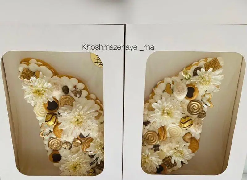 سفارش کیک و شیرینی خوشمزه های ما: دو نیمه کیک پروانه ای با تزیین گل داوودی سفید، شکلات و شیرینی های طلایی.