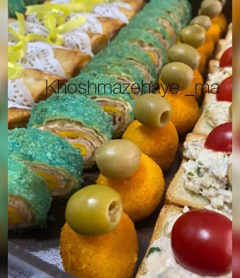 سینی فینگرفود متنوع و خوشمزه شامل رول‌های سبز، تست و اسنک‌های پنیری با زیتون. مزه‌های جذاب برای مهمانی از "خوشمزه های ما".