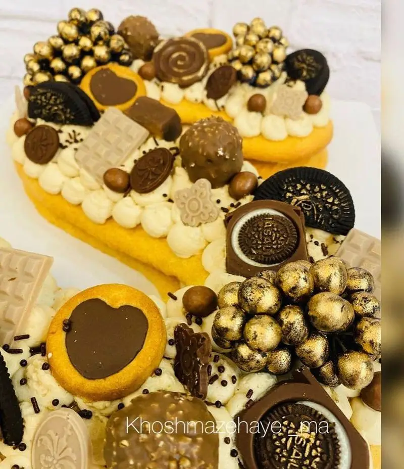 کیک تارت قلبی شکلاتی خاص و خوشمزه، تزئین شده با انواع شکلات، بیسکویت اورئو، گوی‌های طلایی و شیرینی‌های متنوع.