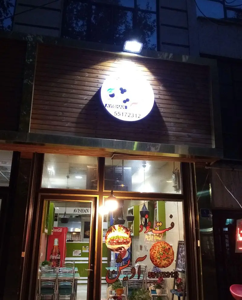 تصویر شبانه از نمای بیرونی فست فود پیتزا آویشن، با تابلوی روشن و شماره تماس 55172312. نمایش همبرگر و پیتزا در ویترین.