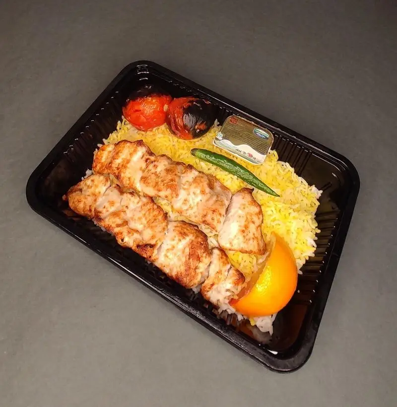 کترینگ لوتوس: چلوکباب جوجه با برنج زعفرانی، گوجه کبابی، فلفل سبز، و کره در ظرف بیرون بر مشکی، مناسب سفارش آنلاین.