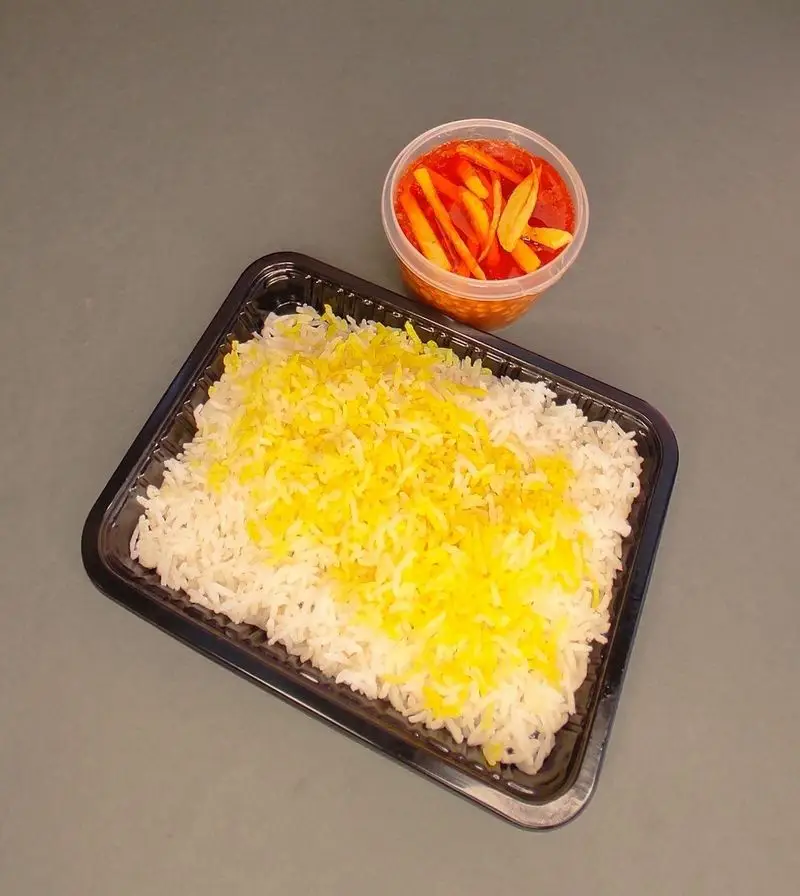 یک پرس برنج زعفرانی و سفید کترینگ لوتوس، آماده برای سرو در سینی مشکی، همراه با ترشی در ظرف جداگانه.