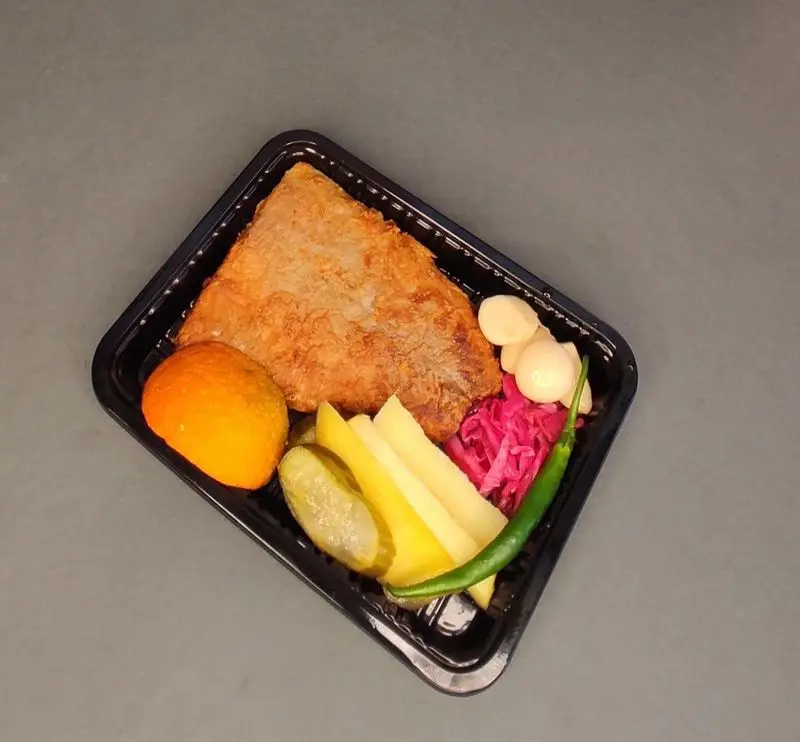 غذای کترینگ لوتوس: فیله ماهی سوخاری با سیب‌زمینی سرخ‌کرده، خیارشور، ترشی کلم و سیر، فلفل و گوجه در ظرف بیرون‌بر.