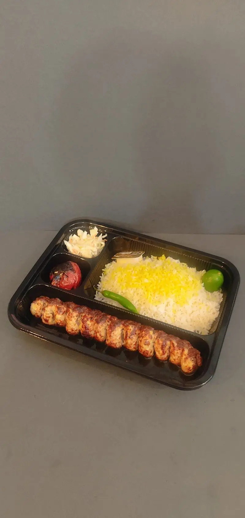 غذای آماده کترینگ لوتوس: چلو کباب کوبیده ممتاز با برنج زعفرانی، گوجه کبابی، سالاد کلم و فلفل در ظرف یکبارمصرف.