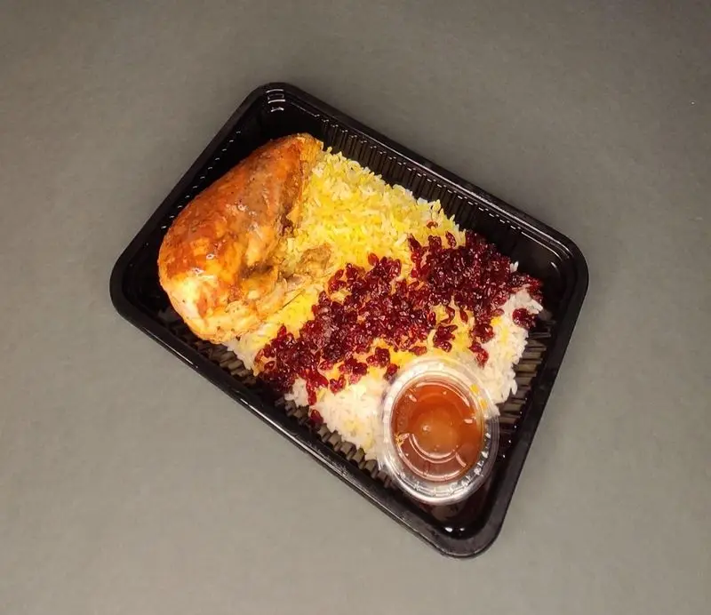 غذای کترینگ لوتوس: ران مرغ، برنج دو رنگ (زعفرانی و سفید) با زرشک، همراه سس در ظرف بیرون‌بر مشکی آماده ارسال.