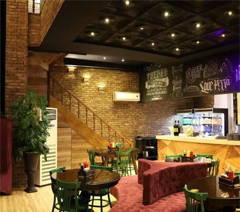 رستوران ایتالیایی پرزو: دکوراسیون داخلی گرم و دلپذیر با دیوارهای آجری، پله چوبی، میز و صندلی سبز، کاناپه قرمز و کانتر شیک.