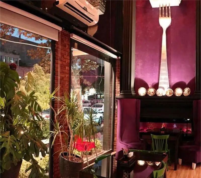 فضای دلنشین و دکوراسیون چشمگیر رستوران ایتالیایی پرزو: دیوار بنفش با چنگال نورانی بزرگ، صندلی‌های بنفش و سبز و نمایی رو به خیابان.