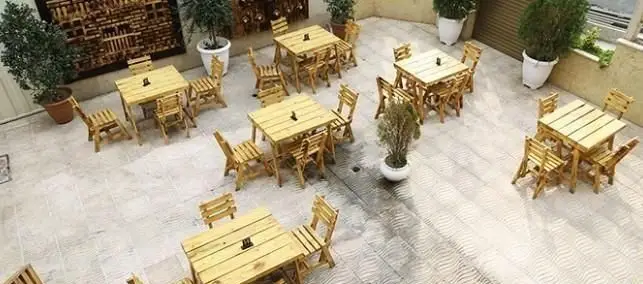 محیط دلباز و آرامش‌بخش پیتزایی ایرانویچ با چیدمان شیک میز و صندلی‌های چوبی روشن در فضای باز، مناسب دورهمی‌های خانوادگی و دوستانه.