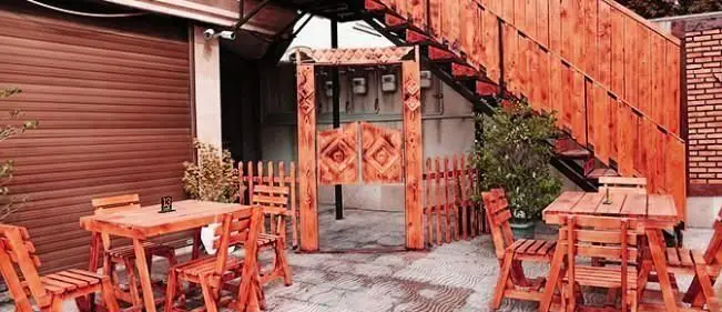 فضای باز و حیاط پیتزایی ایران ویچ با میز و صندلی‌های چوبی قهوه‌ای، مناسب صرف انواع پیتزا و غذا در محیطی آرام و دلپذیر.