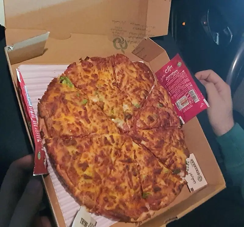 نمایی از پیتزا رسپینا داغ و لذیذ، برش خورده در جعبه تحویل. این پیتزای خوشمزه با سس مخصوص، آماده سرو و یک غذای آماده عالی است.