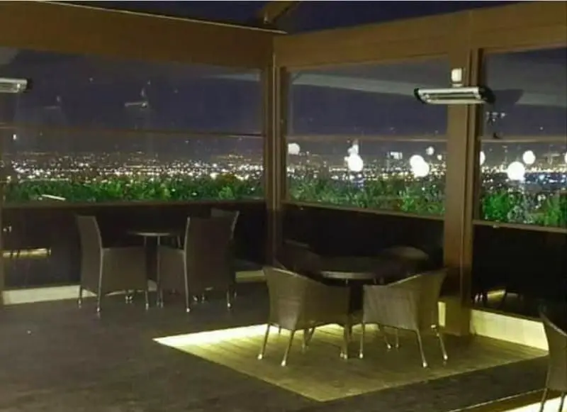 رستوران فرنگی بامیکا لانژ با منظره شب خیره کننده شهر، فضای باز دنج و میز و صندلی‌های شیک برای تجربه‌ای دلنشین از شام و کافه.