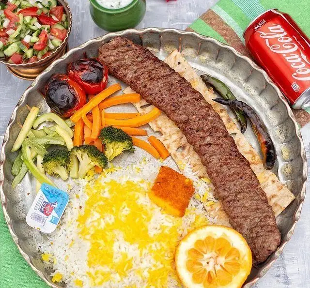 کباب کوبیده مخصوص رستوران گیلار در سینی فلزی با چلو زعفرانی، گوجه، فلفل، هویج، کلم بروکلی، پرتقال و کره، یک ضیافت ایرانی.