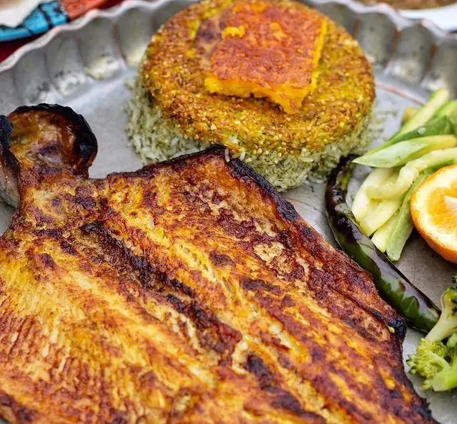 ماهی کباب طلایی با سبزی پلو ته دیگی خوشرنگ و مخلفات تازه، یک غذای اصیل ایرانی از رستوران گیلار.
