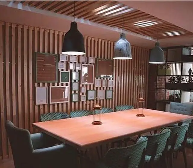 فضای داخلی کافه رستوران ویراک با میز بزرگ چوبی، صندلی‌های سبز، دیوارهای چوبی و آویزهای شیک، محیطی دنج و مدرن.