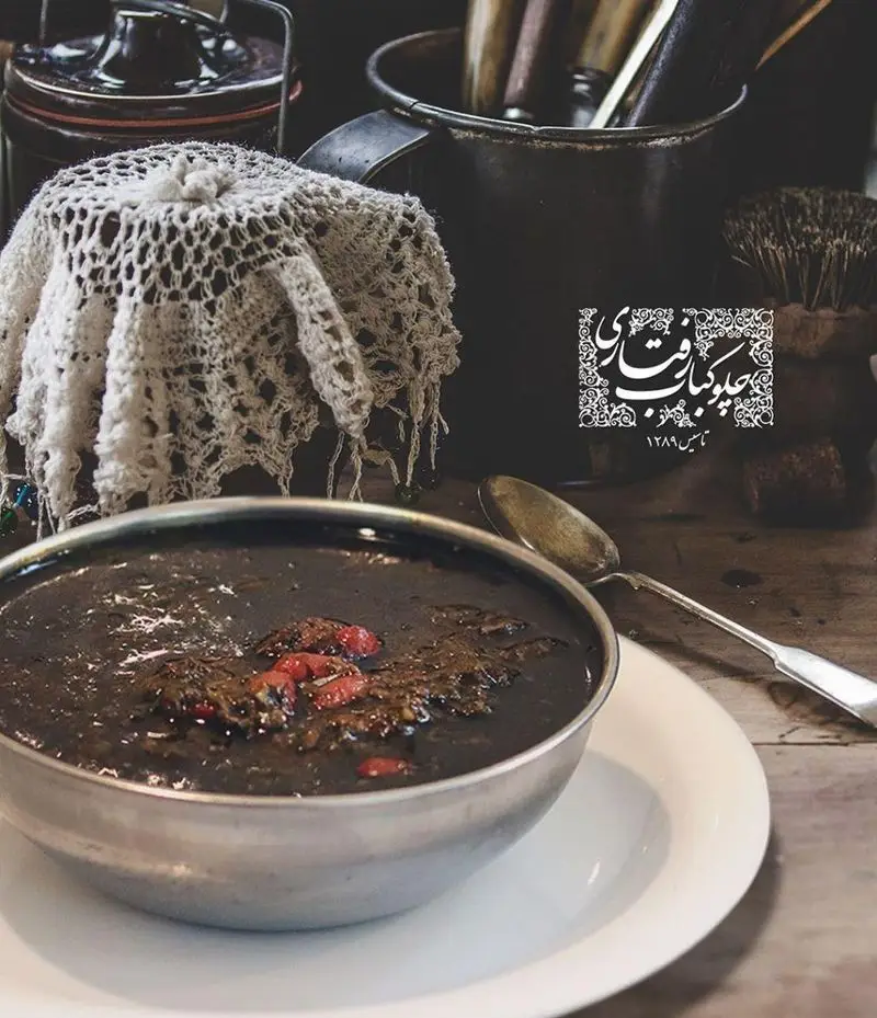 خورشت اصیل ایرانی در رستوران رفتاری، سرو شده در کاسه‌ای فلزی روی میز چوبی با دکوری سنتی. تصویری از آشپزی قدیمی ایران.