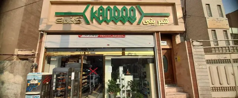 فروشگاه نان شیرینی کندو با نمای بیرونی جذاب، تابلوی Kandoo و اطلاعات تماس (تلفن و اینستاگرام shirini_kandoo_) برای خرید نان و شیرینی تازه.