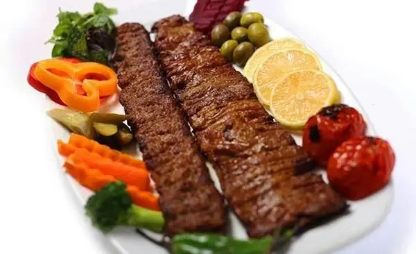 کباب کوبیده مخصوص آبان، یک بشقاب غذای لذیذ ایرانی با مخلفات کامل شامل گوجه، لیمو، زیتون، ترشی و سبزیجات.