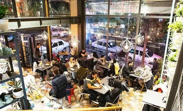 فضای داخلی دنج و مدرن کافه رستوران البا در شب با حضور مشتریان. مکانی عالی برای دورهمی و صرف غذا و نوشیدنی.