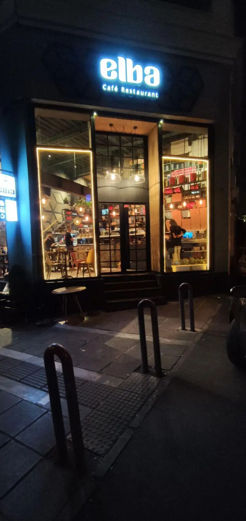 نمای بیرونی کافه رستوران البا در شب با تابلوی نئونی درخشان و پنجره های بزرگ که دکوراسیون داخلی و نورپردازی گرم را نشان می دهد.