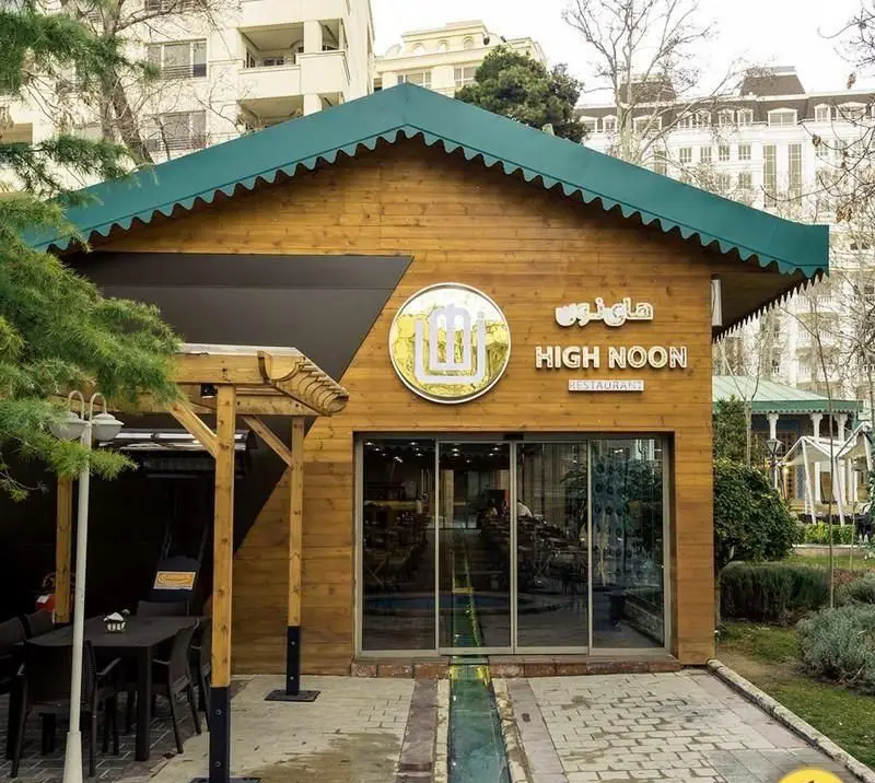 تصویری از نمای بیرونی رستوران های‌نون، با معماری چوبی، سقف سبز و لوگوی برجسته. شامل فضای غذاخوری در فضای باز و محیطی دلنشین.