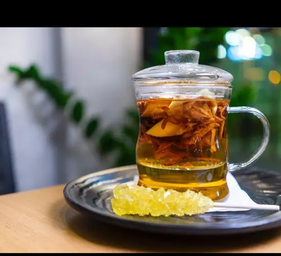 دمنوش شفابخش میوه‌ای و دارچین در ماگ شیشه‌ای کافه بوتیک زی بن، همراه با نبات زعفرانی، تجربه‌ای دلنشین و آرامش‌بخش.