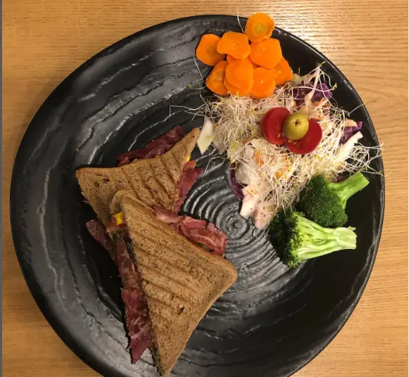 بشقاب کامل ساندویچ گوشت دودی با نان تست، سالاد تازه سبزیجات، هویج و بروکلی بخارپز از کافه بوتیک زی بن.