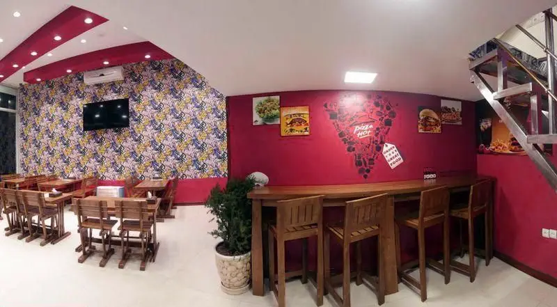 فضای داخلی شیک و مدرن رستوران پیتزا هات با دیوارهای قرمز و طرح‌دار، همراه با میز و صندلی‌های چوبی و پوسترهای غذا.