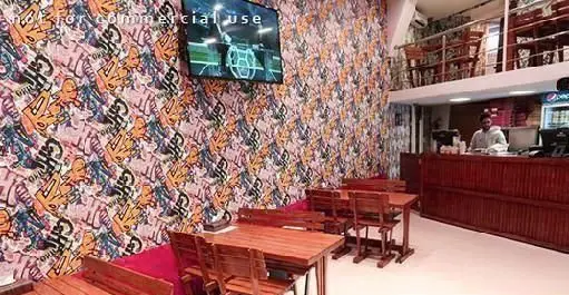 فضای داخلی رستوران پیتزا هات با دکوراسیون دیوار طرح گرافیکی، میز و صندلی چوبی، پیشخوان سفارش غذا، تلویزیون و سالن پذیرایی.