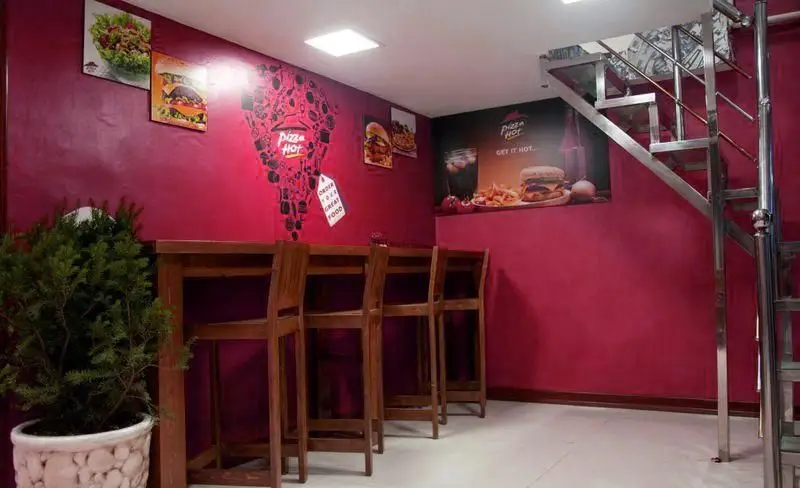 فضای داخلی جذاب رستوران فست فود پیتزا هات با دیوارهای صورتی، میزهای چوبی بلند و پوسترهای اشتهاآور غذا.