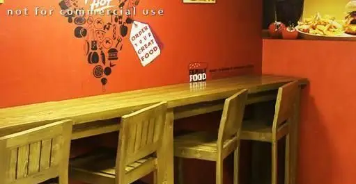 فضای داخلی دلپذیر رستوران پیتزا هات با میز و صندلی‌های چوبی، دیوار قرمز با نقوش فست فود و شعار "Order Your Great Food".