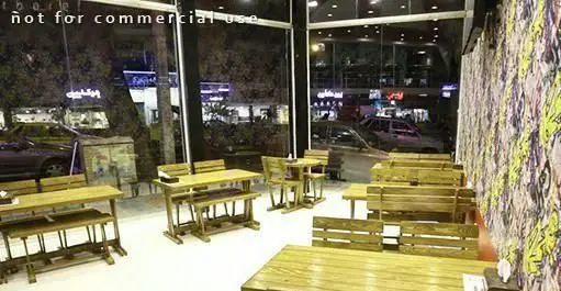 فضای داخلی رستوران پیتزا هات با میز و نیمکت‌های چوبی شیک و دیوارهای طرح‌دار. نمای شب شهر از پشت پنجره بزرگ.