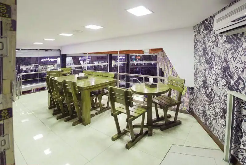 تصویری از فضای داخلی مدرن و دنج رستوران پیتزا هات، شامل میز و صندلی‌های چوبی سبزرنگ، دیوار با طرح گرافیتی، نورپردازی سقفی و منظره خیابان از پنجره‌های بزرگ.