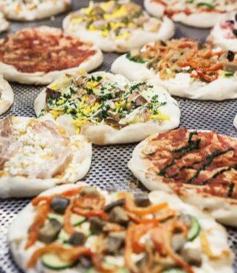 مجموعه‌ای از مینی پیتزاهای رنگارنگ و متنوع با انواع تاپینگ‌های تازه مانند سبزیجات، پنیر و قارچ، آماده پخت در سام استریت تجریش.
