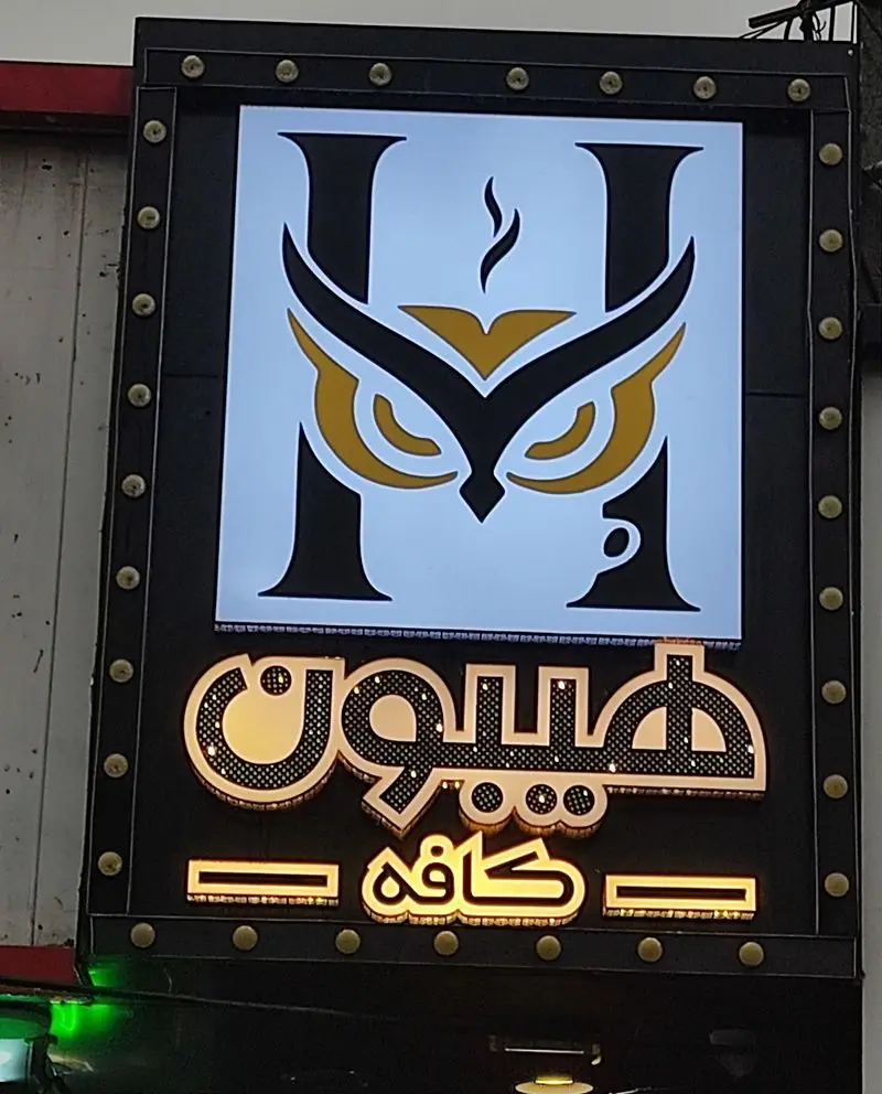 تابلو نئونی کافه هیبون با لوگوی تلفیقی جغد، فنجان قهوه و حرف H، همراه با نام درخشان طلایی برای جذب مشتریان در شب.