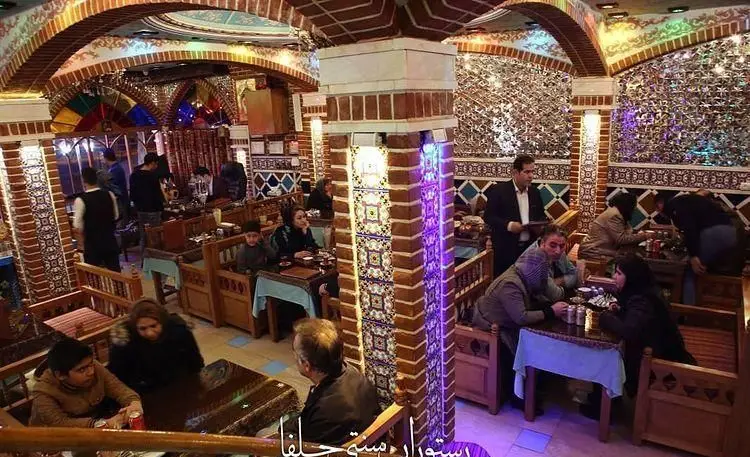 فضای دلنشین رستوران سنتی جلفا با دکوراسیون اصیل ایرانی، شامل طاق‌های آجری، آینه‌کاری، کاشی‌کاری زیبا و مهمانانی در حال صرف غذا.