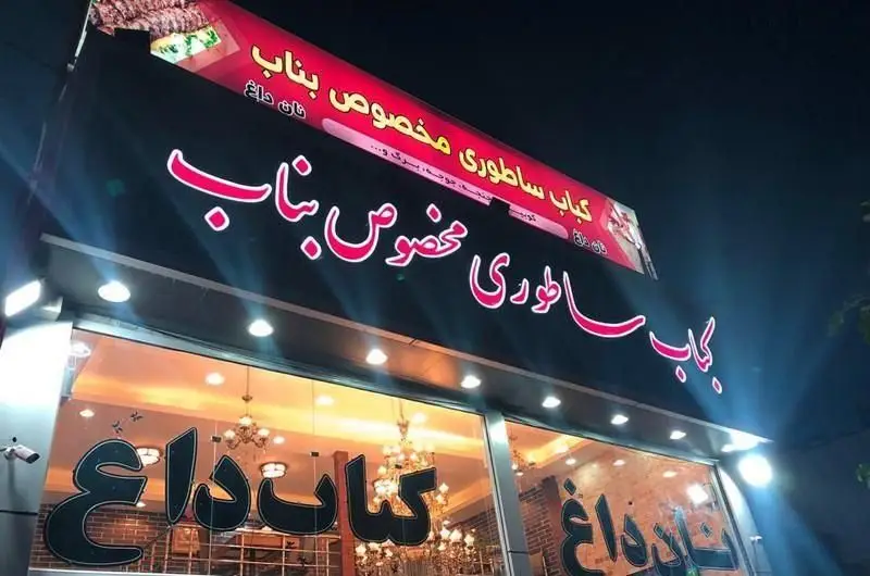 نمای شبانه کبابی کباب ساطوری مخصوص بناب با تابلوهای روشن، شامل کلمات کباب داغ و نان داغ، جذاب و اشتهاآور.