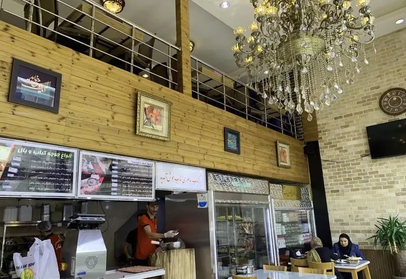 فضای داخلی رستوران کبابی کباب ساطوری مخصوص بناب، شامل منوی متنوع کباب‌ها، آشپز در حال آماده‌سازی و مشتریان.