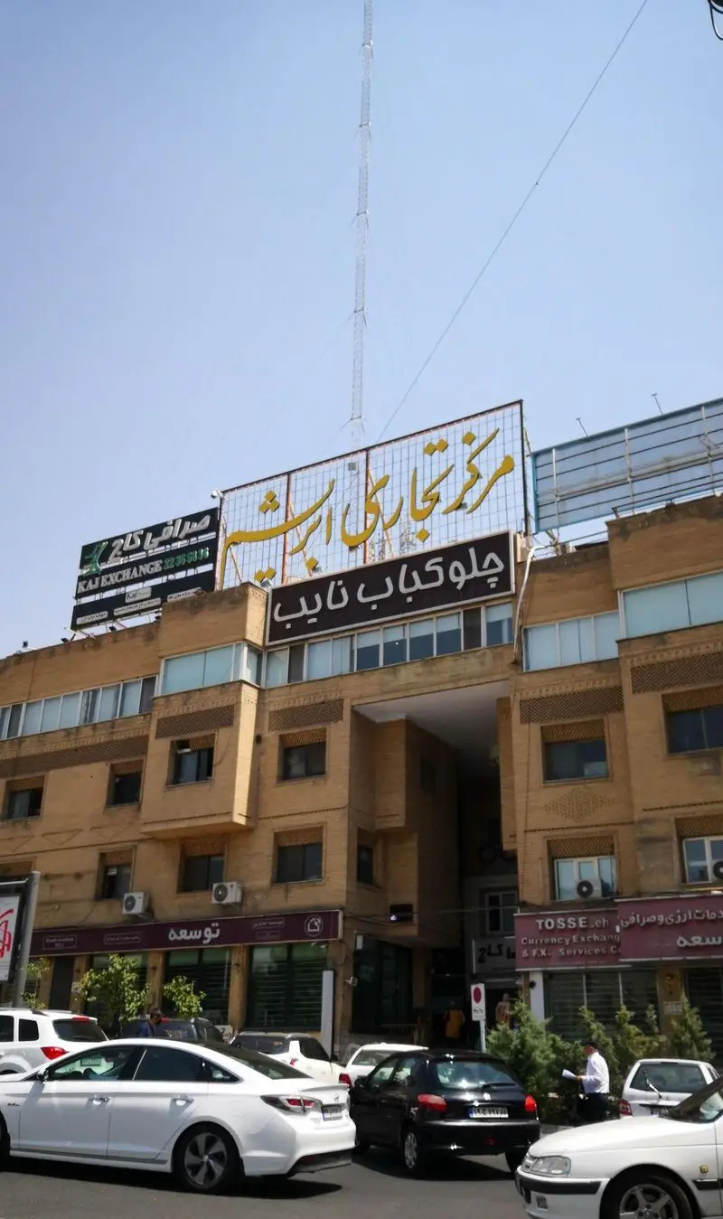 تابلو و نمای بیرونی رستوران معروف چلو کباب نایب در تهران، واقع در مرکز تجاری ارشت با صرافی کاج و ماشین‌ها در خیابان.