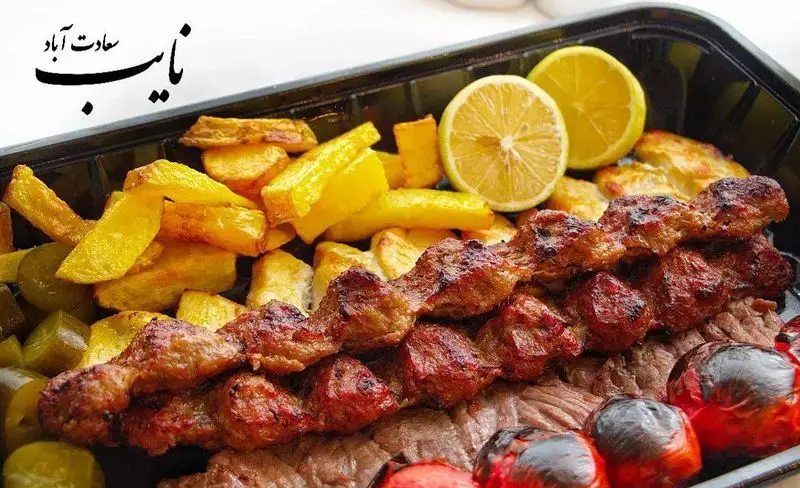 چلو کباب نایب سعادت آباد: بشقاب کباب با سیب زمینی سرخ کرده، لیمو، گوجه کبابی و خیارشور، یک وعده غذایی کامل و لذیذ.