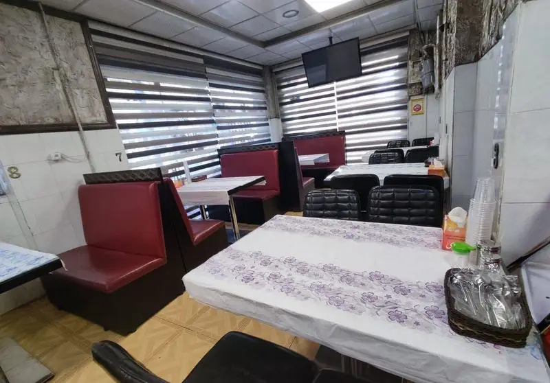 فضای داخلی رستوران حامدی با میزهای غذاخوری مرتب، صندلی‌های راحتی قرمز و مشکی، پرده‌های مدرن و تلویزیون برای محیطی دلپذیر.